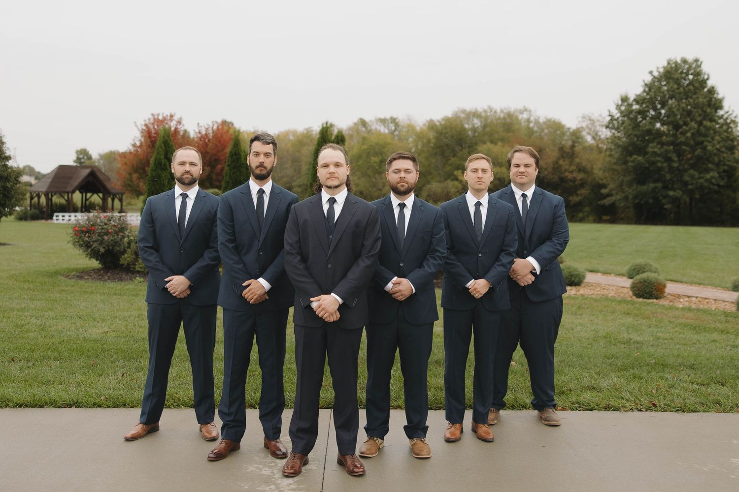 Groomsmen in navy suits and brown shoes show off their colorful socks in a playful outdoor photo.
