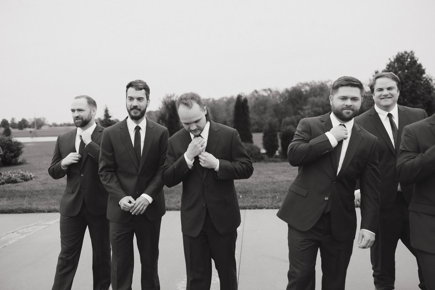 A group of groomsmen in black suits pose playfully in a sequence of candid shots outdoors.