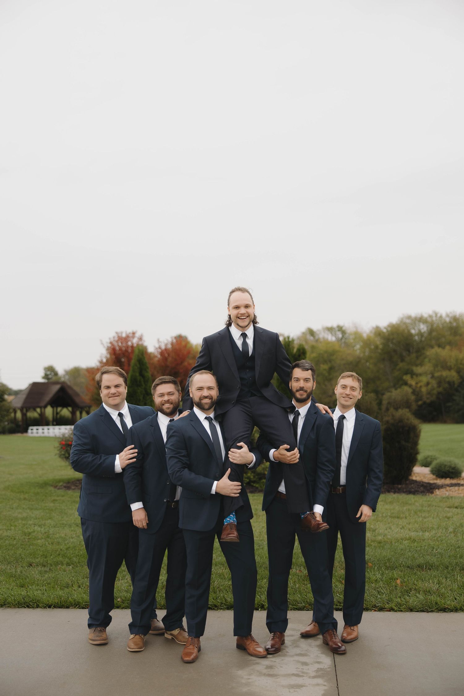 Groomsmen in navy suits and brown shoes pose casually on a stone pathway outdoors.