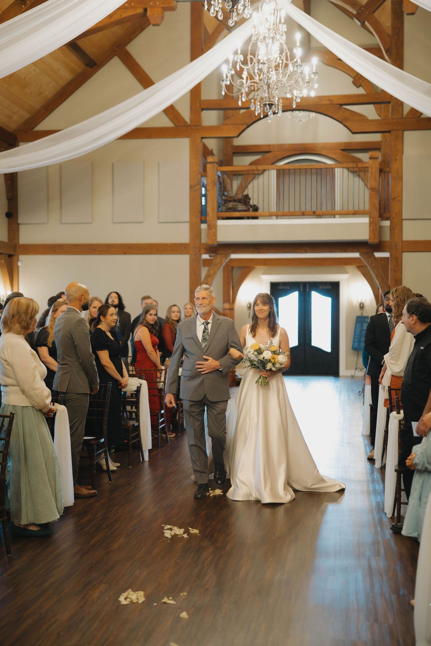 Wedding guests gathered in an elegant reception hall with wooden beams and white drapes hanging from the ceiling.