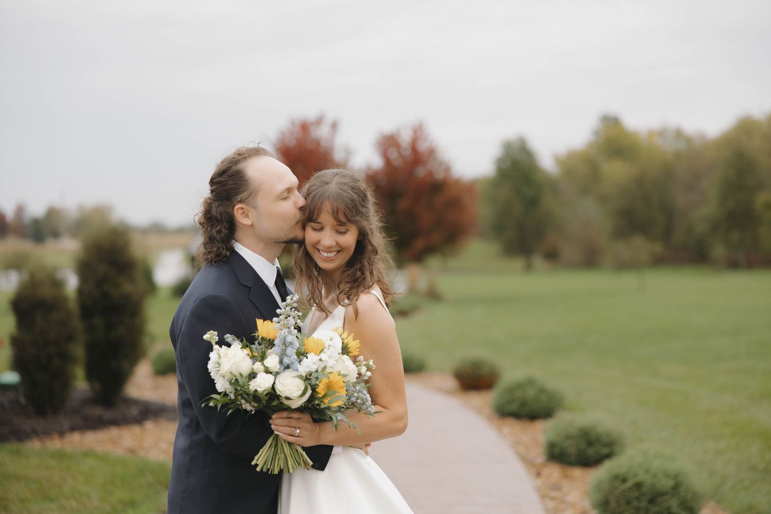 A couple shares intimate moments during their outdoor wedding photoshoot in a scenic green field.