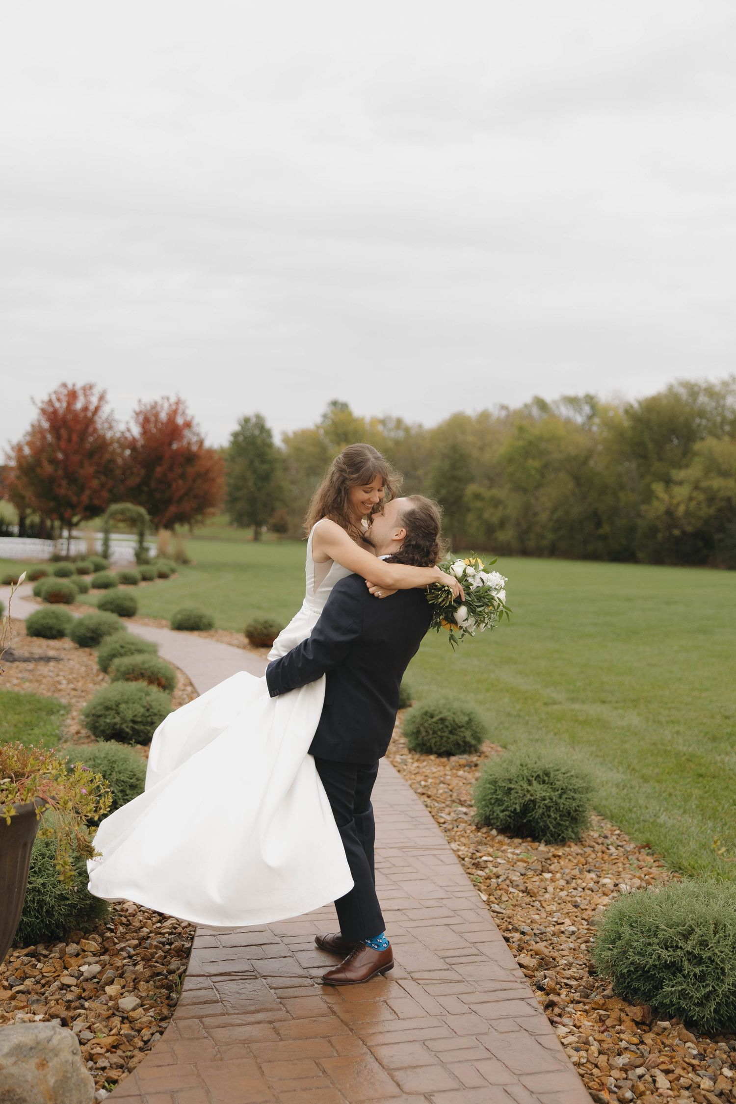 A playful dance dip captured on a landscaped stone path during an autumn wedding.