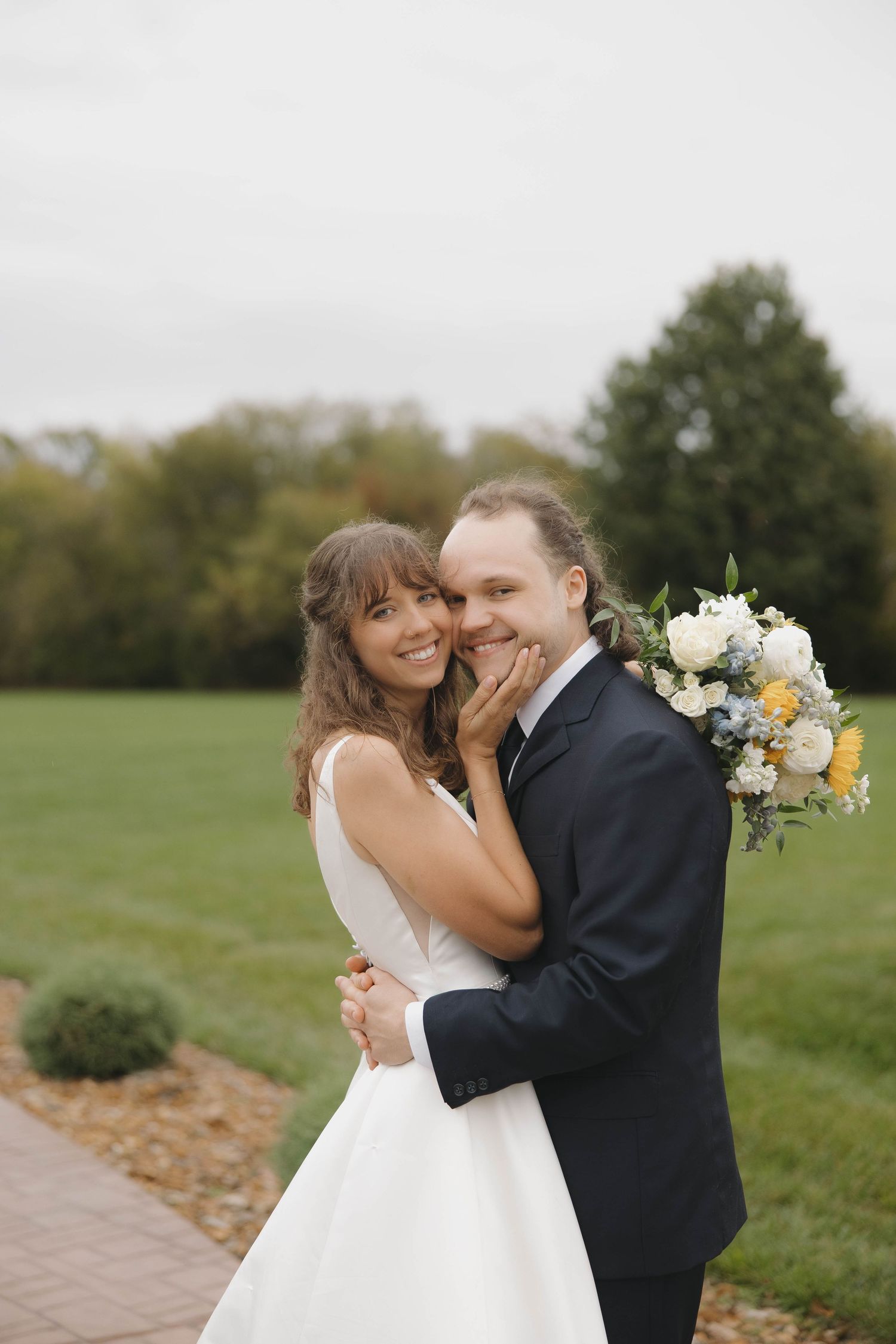 Happy couple sharing an intimate moment outdoors with a bouquet of white and yellow flowers.