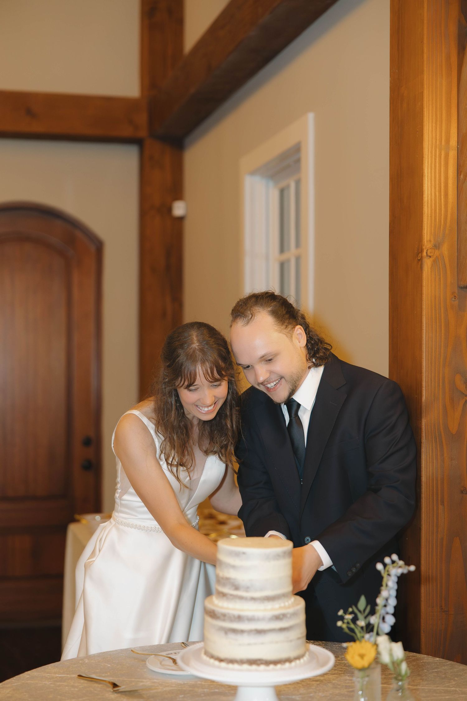 A couple shares an intimate moment while cutting their simple white wedding cake in a rustic wooden interior.