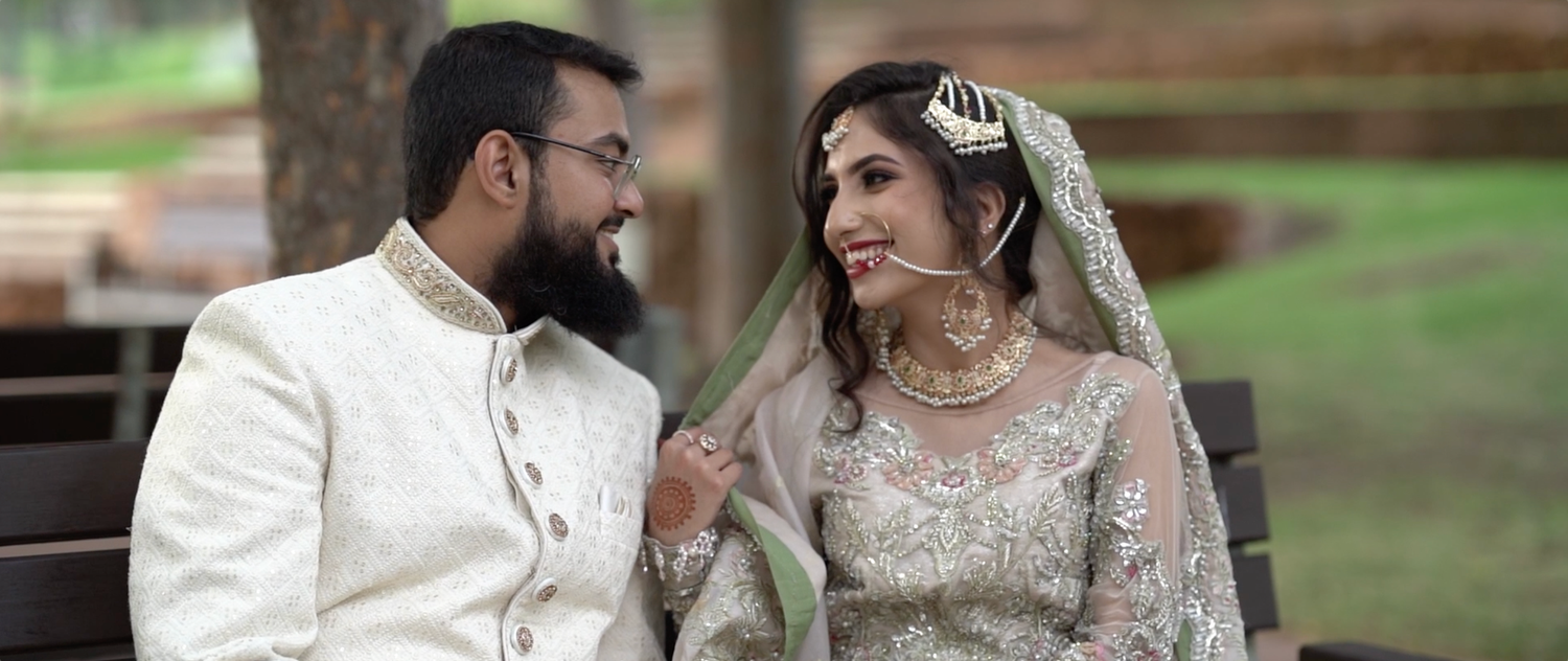 Couple in traditional South Asian wedding attire sharing an intimate moment outdoors.
