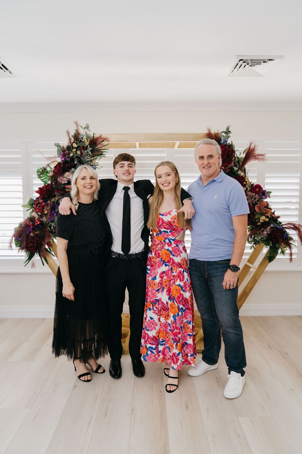 Group photo with wooden floral arch backdrop in bright indoor setting.