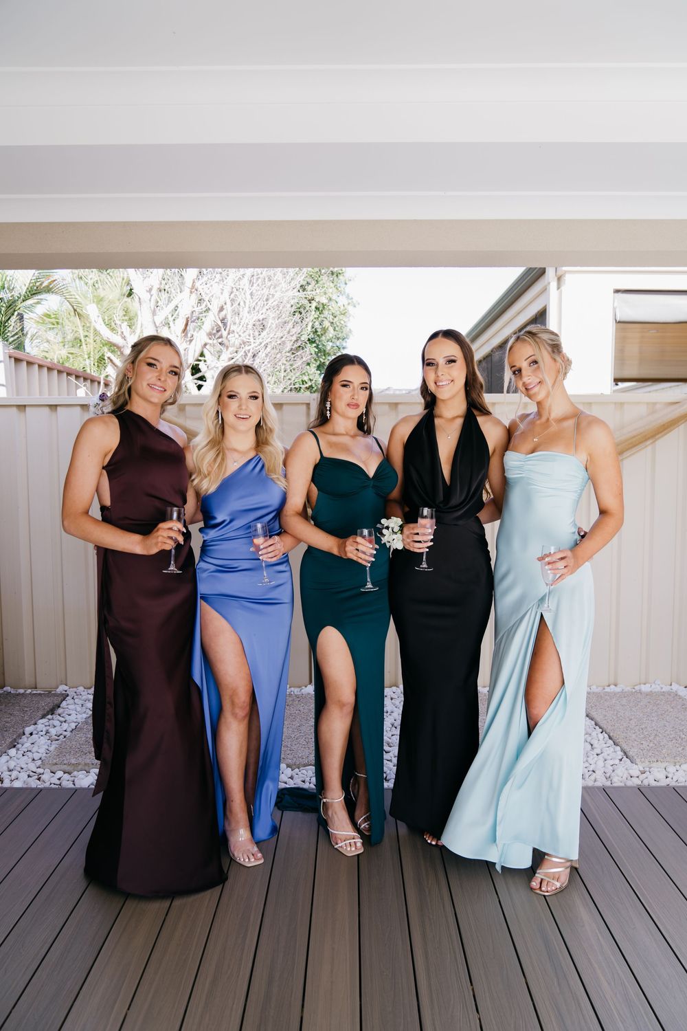 Group in formal attire posing together on wooden deck.