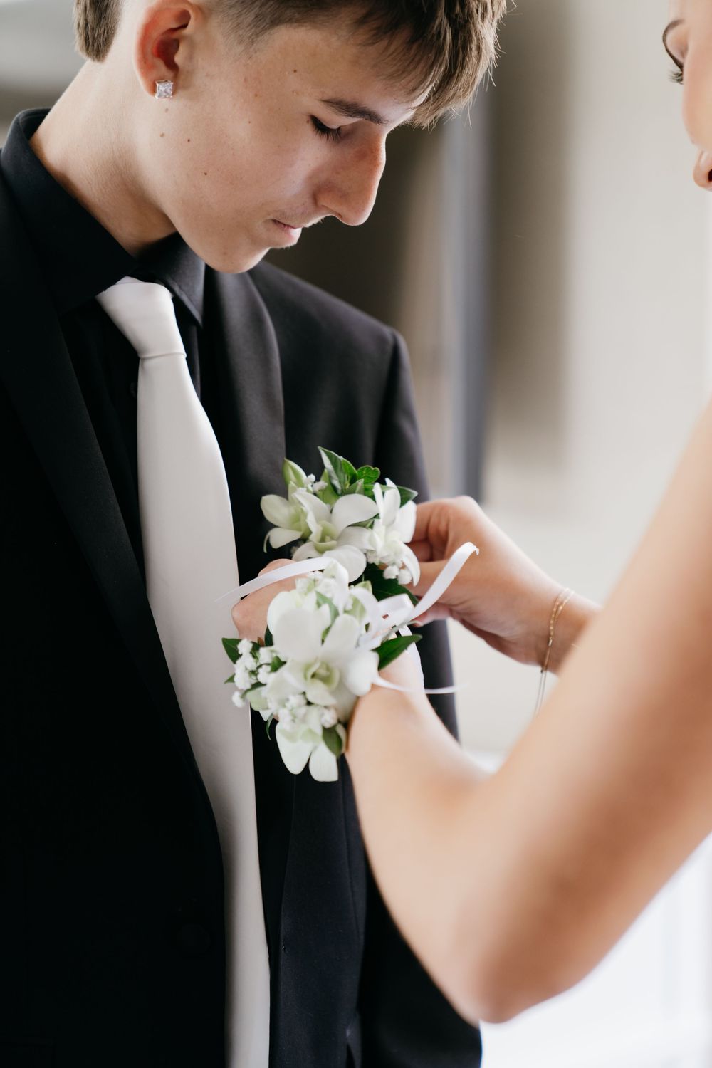 Close-up of white floral boutonniere being pinned to black suit jacket.