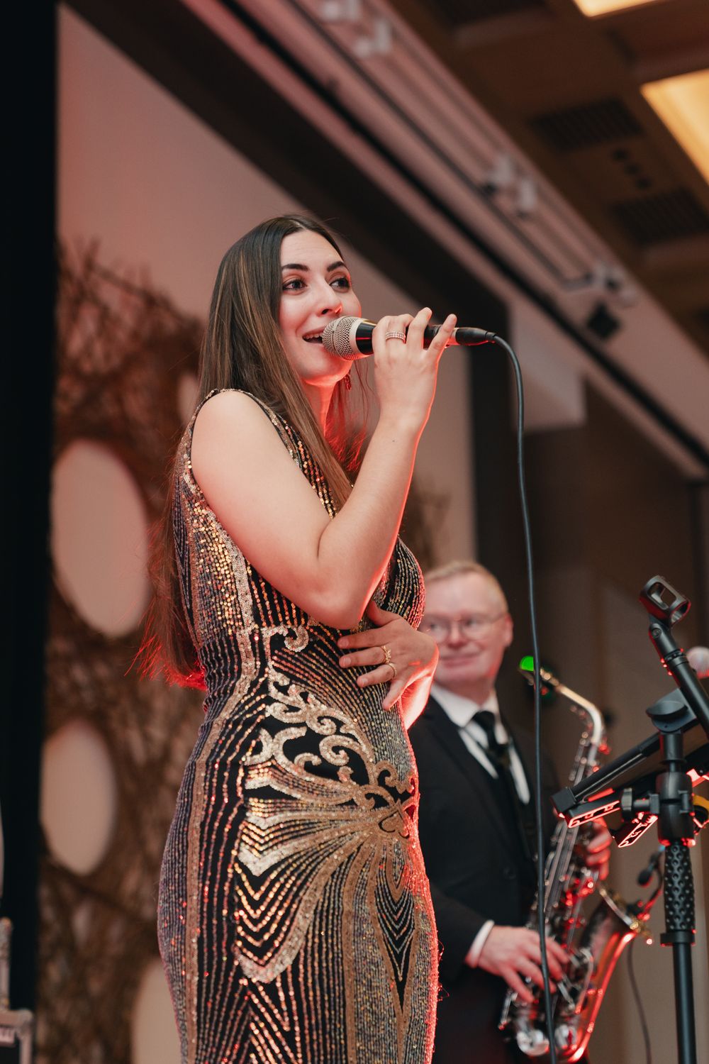 A performer in a sequined dress sings on stage during an event.