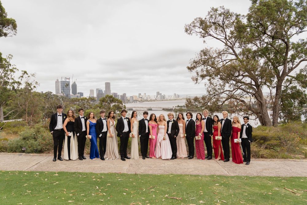 Large formal wedding party posed for photos with city skyline visible in background.