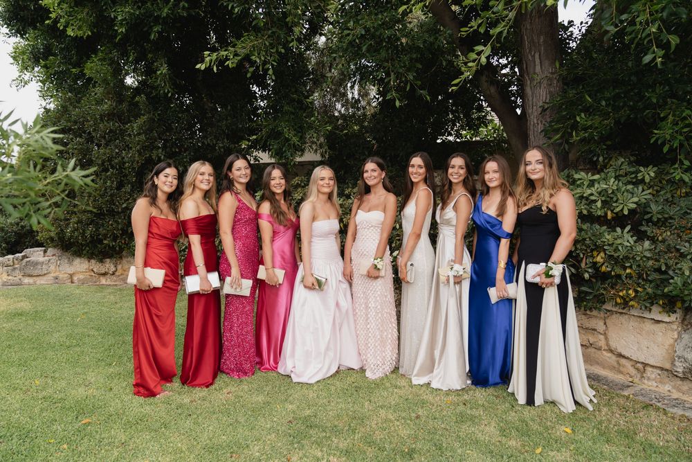 Wedding party members in red, pink and white dresses lined up outdoors for a group photo.