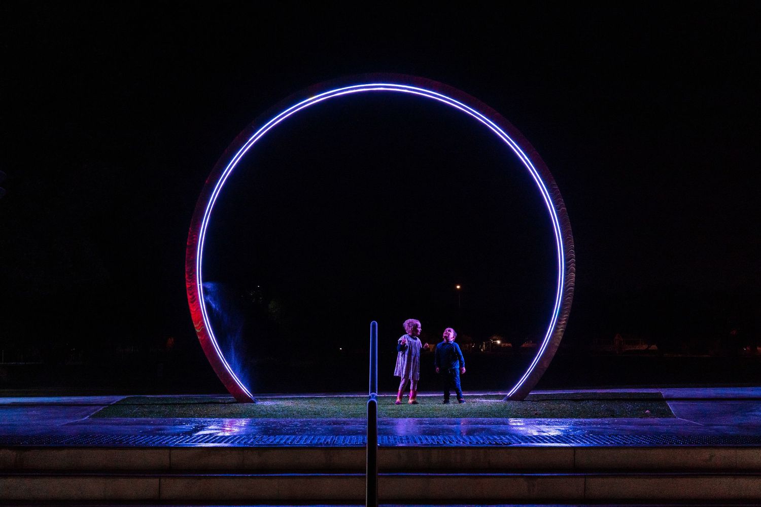 Large illuminated blue and purple neon circle installation glowing in the darkness.