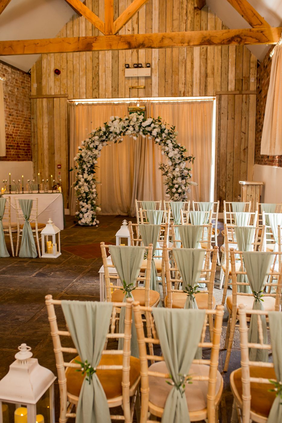 Rustic barn wedding venue with wooden beams and white chairs decorated with mint green sashes.
