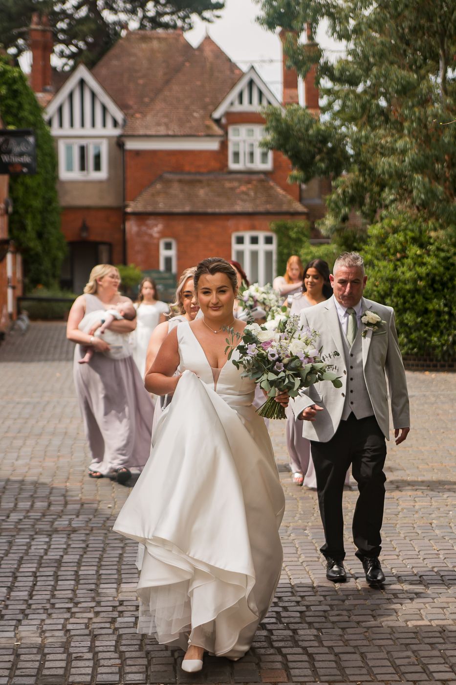 Joyful wedding party celebration on cobblestone courtyard with manor house backdrop.