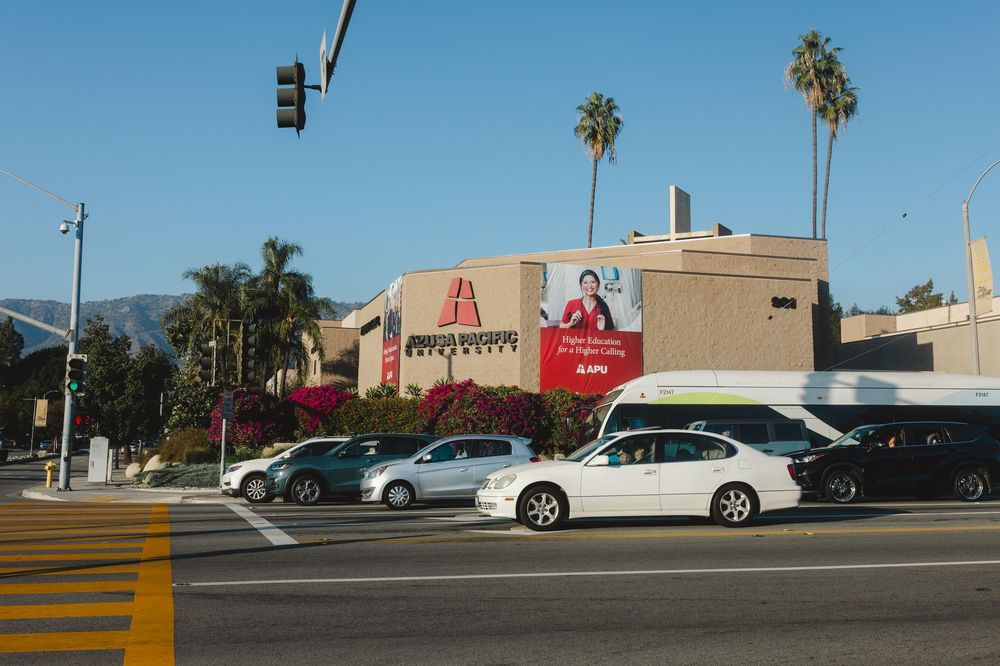 A panoramic view of a commercial street with palm trees, traffic lights, and various retail buildings in a suburban area.