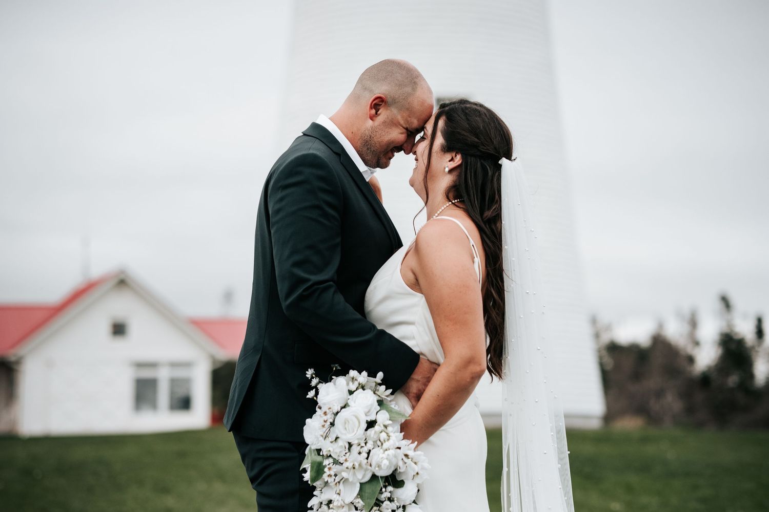 A romantic wedding couple shares an intimate moment in front of a rustic white barn on their special day.