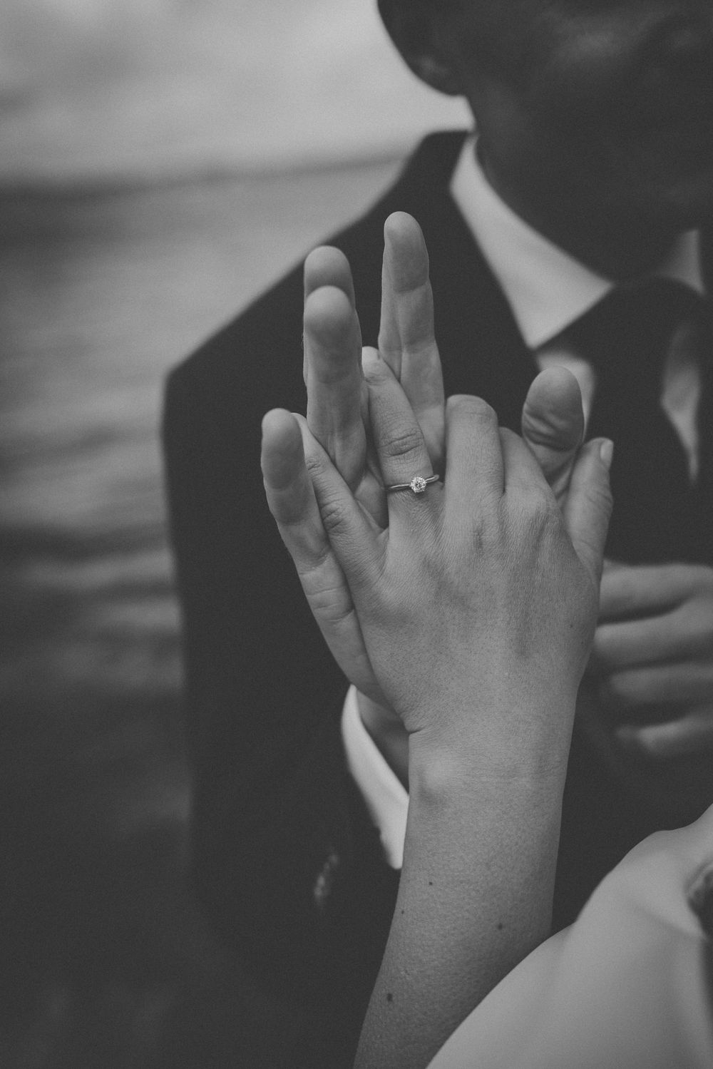 Close-up of wedding rings and clasped hands in black and white.