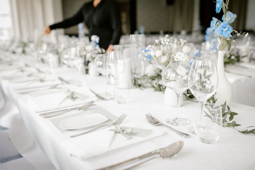 Elegant wedding reception tables decorated with white linens, blue hydrangeas, and crystal glassware create a sophisticated setting.