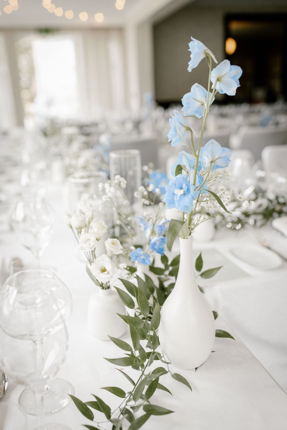 Elegant wedding table centerpiece with delicate blue and white flowers in a frosted vase.