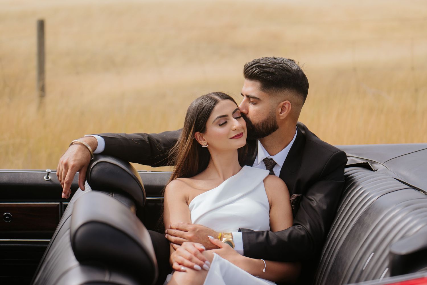 Romantic couple embraces on wooden bench against golden field during sunset photoshoot.