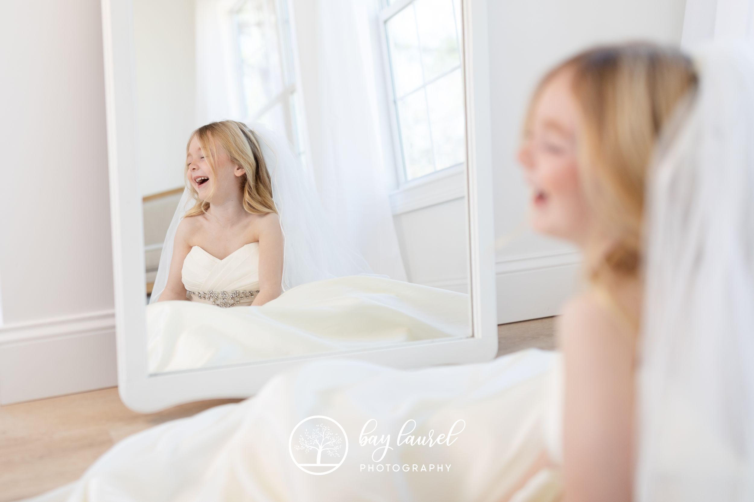 A bride in white sits near a mirror creating a dreamy reflection in natural light.