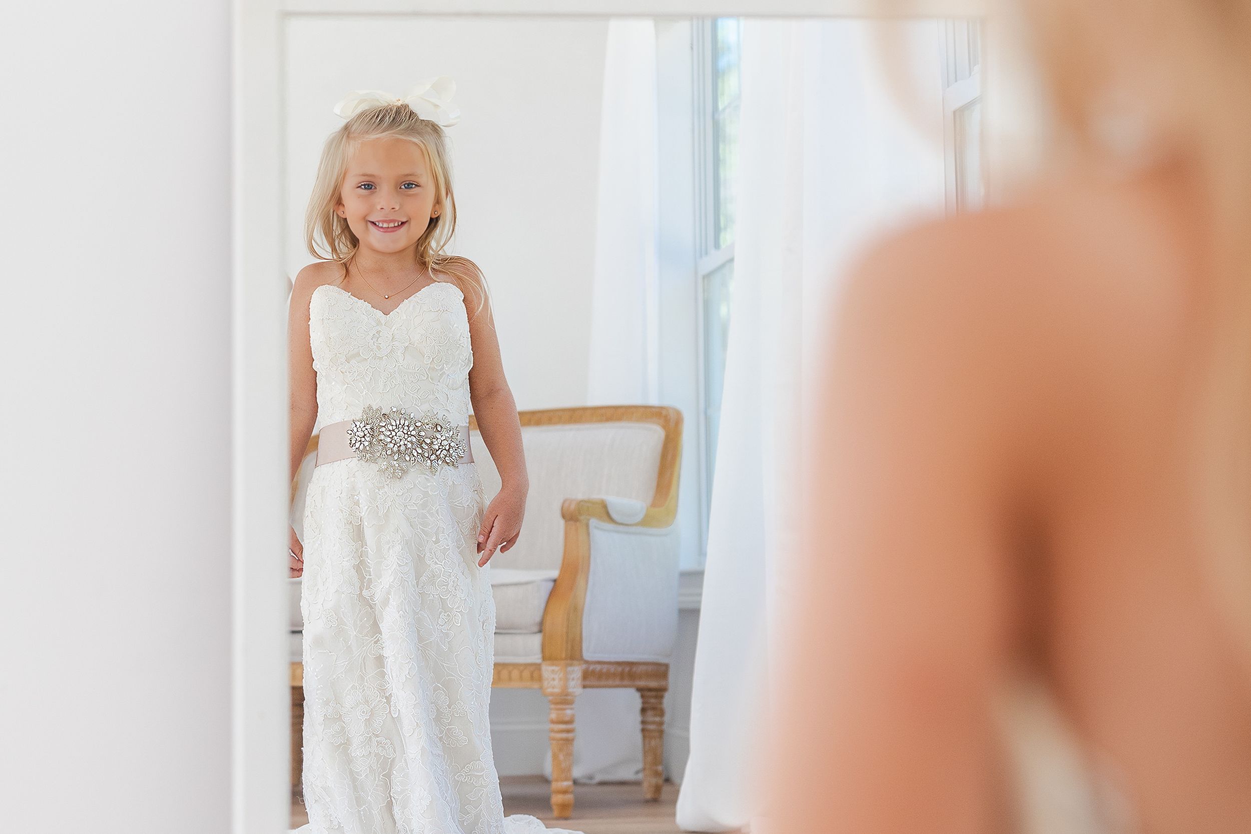 White lace dress flows elegantly in natural window light during bridal preparation.