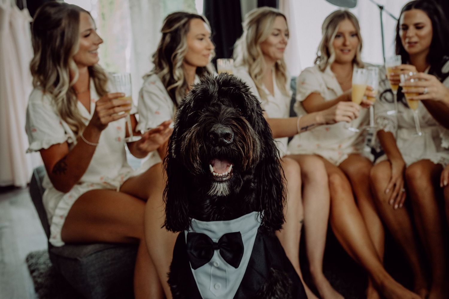 A group of people in white dresses sit together laughing and socializing at a bridal party gathering.