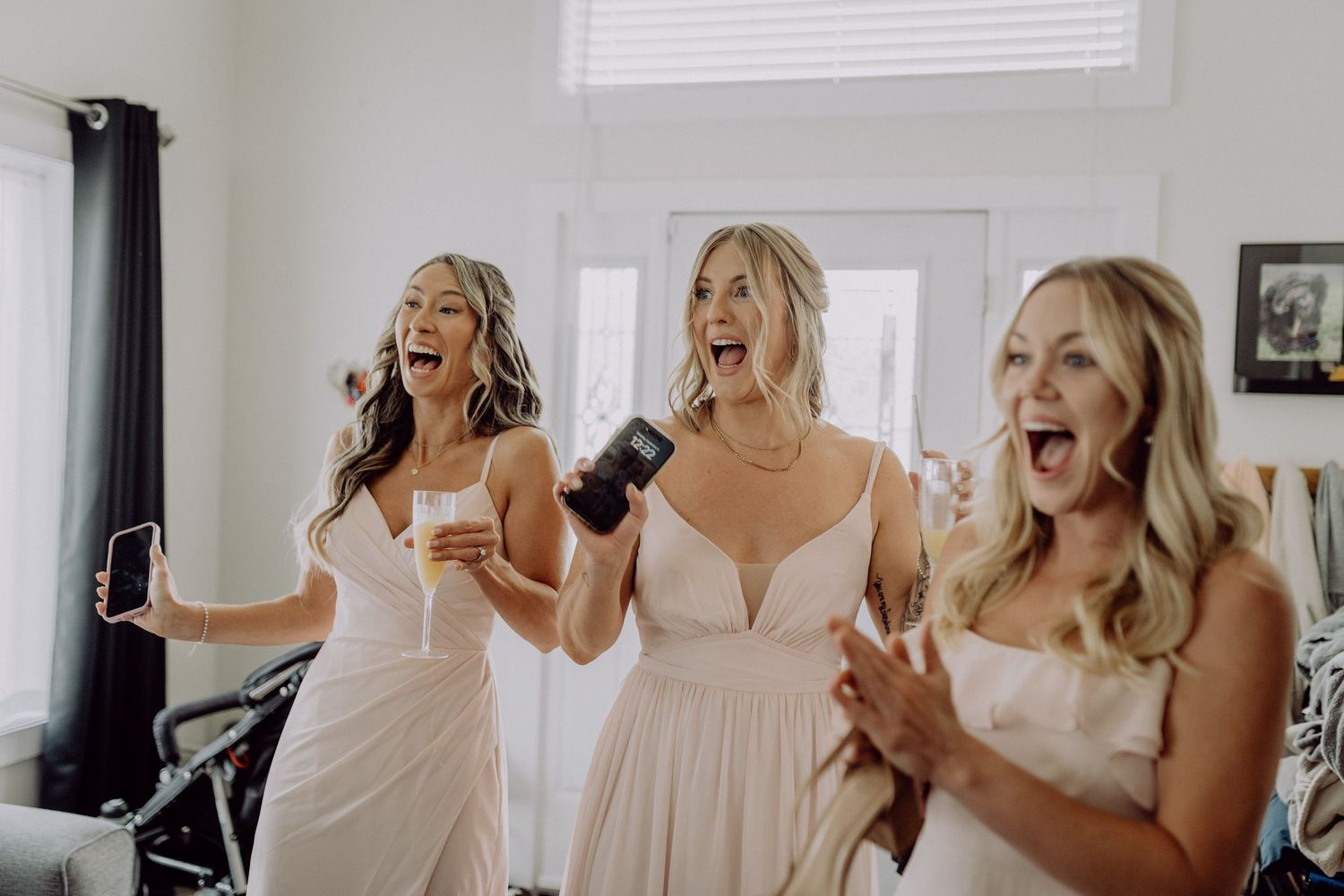 A group of bridesmaids in white robes laugh and dance together while getting ready on wedding day.