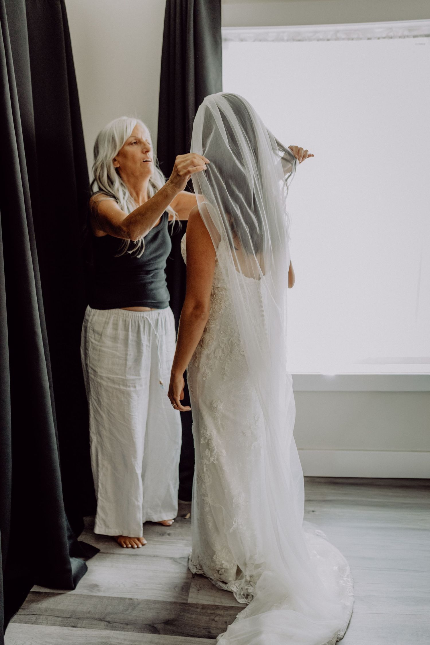 A wedding dress fitting session shows someone adjusting the delicate lace details of a white bridal gown.