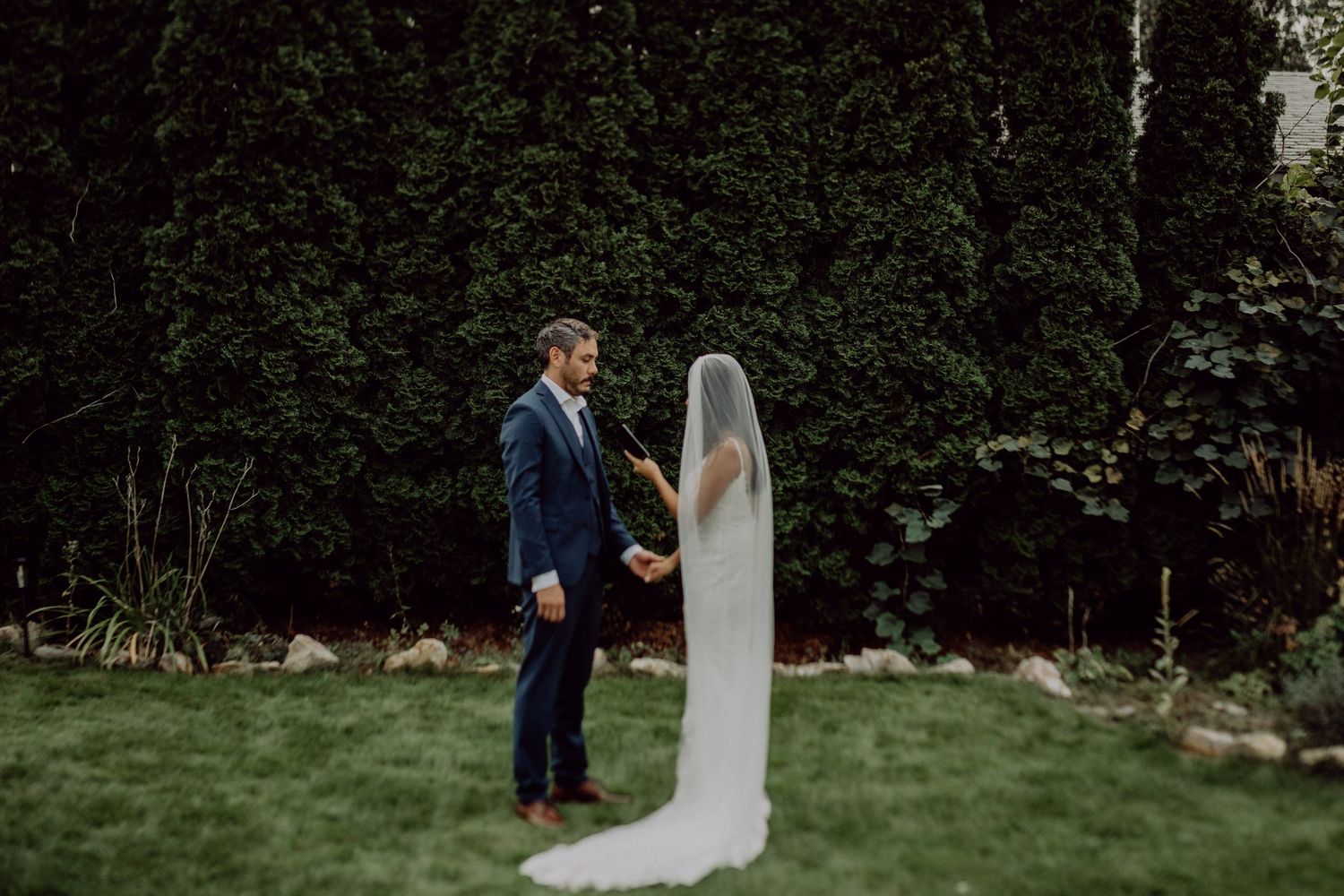 A couple in wedding attire shares an intimate moment in a lush garden setting.