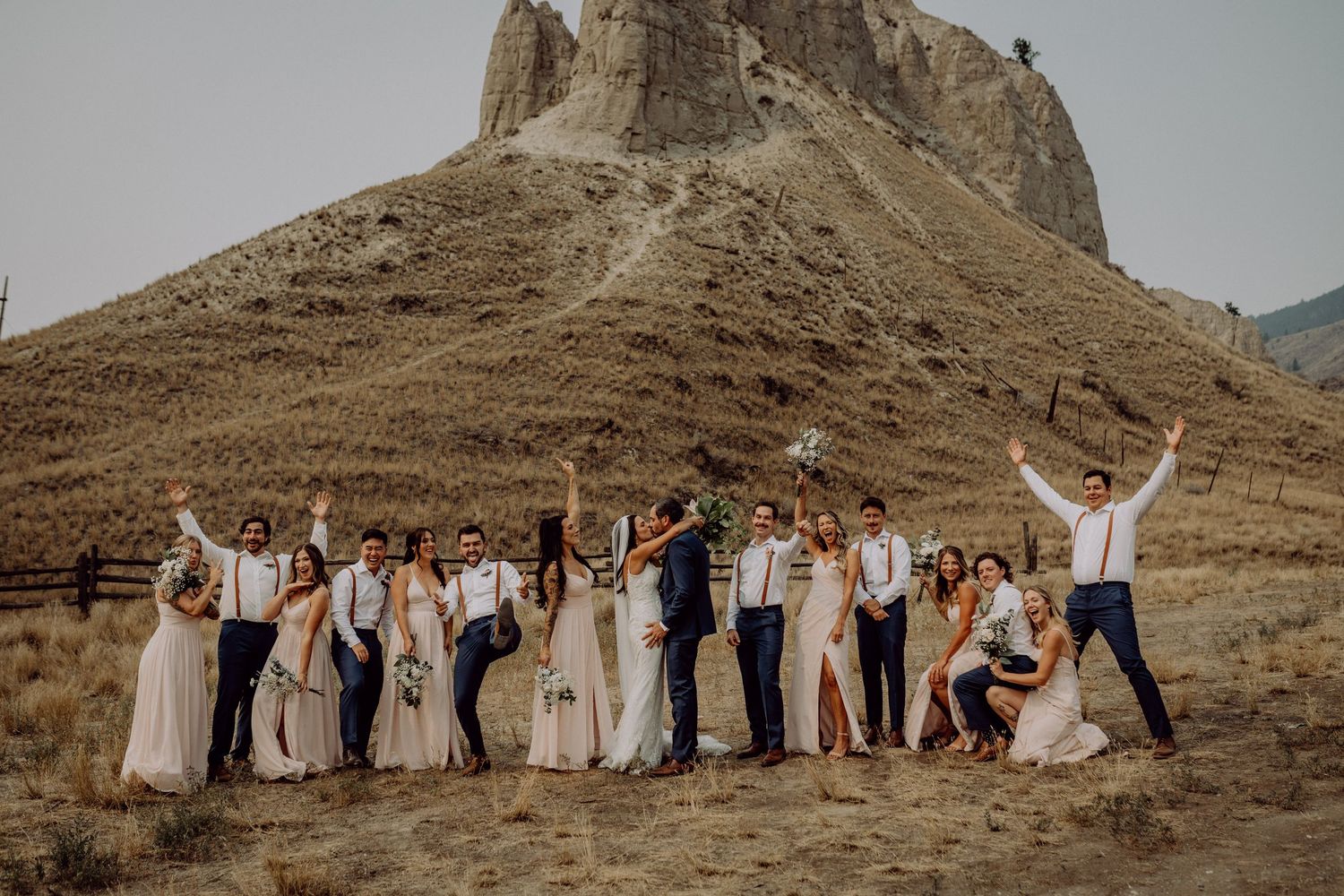 Wedding party poses together against dramatic desert mountain landscape at sunset.