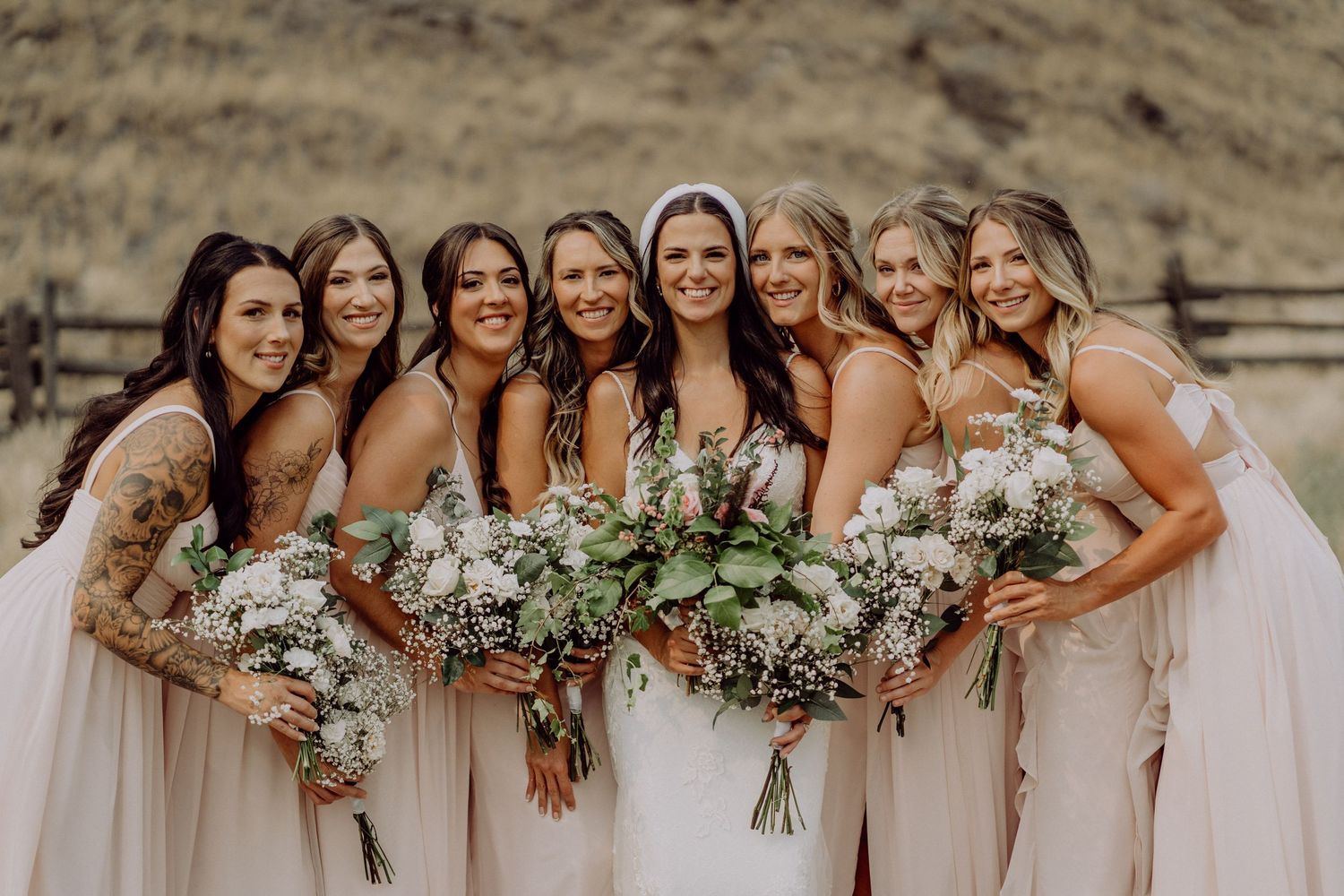 A group wearing blush pink bridesmaid dresses pose together while holding white floral bouquets.