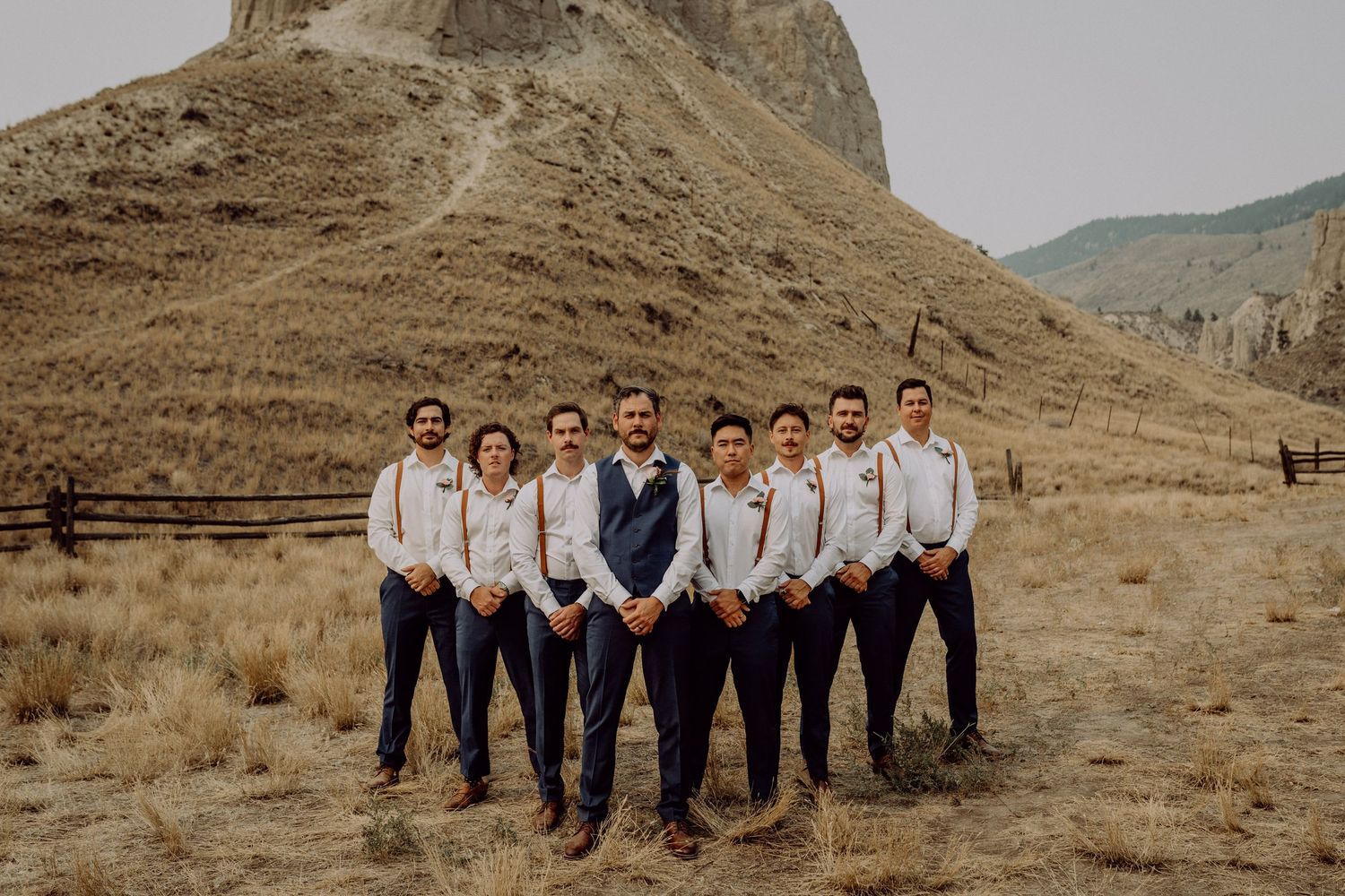 A wedding party poses together against a backdrop of dramatic desert mountains and rugged terrain.