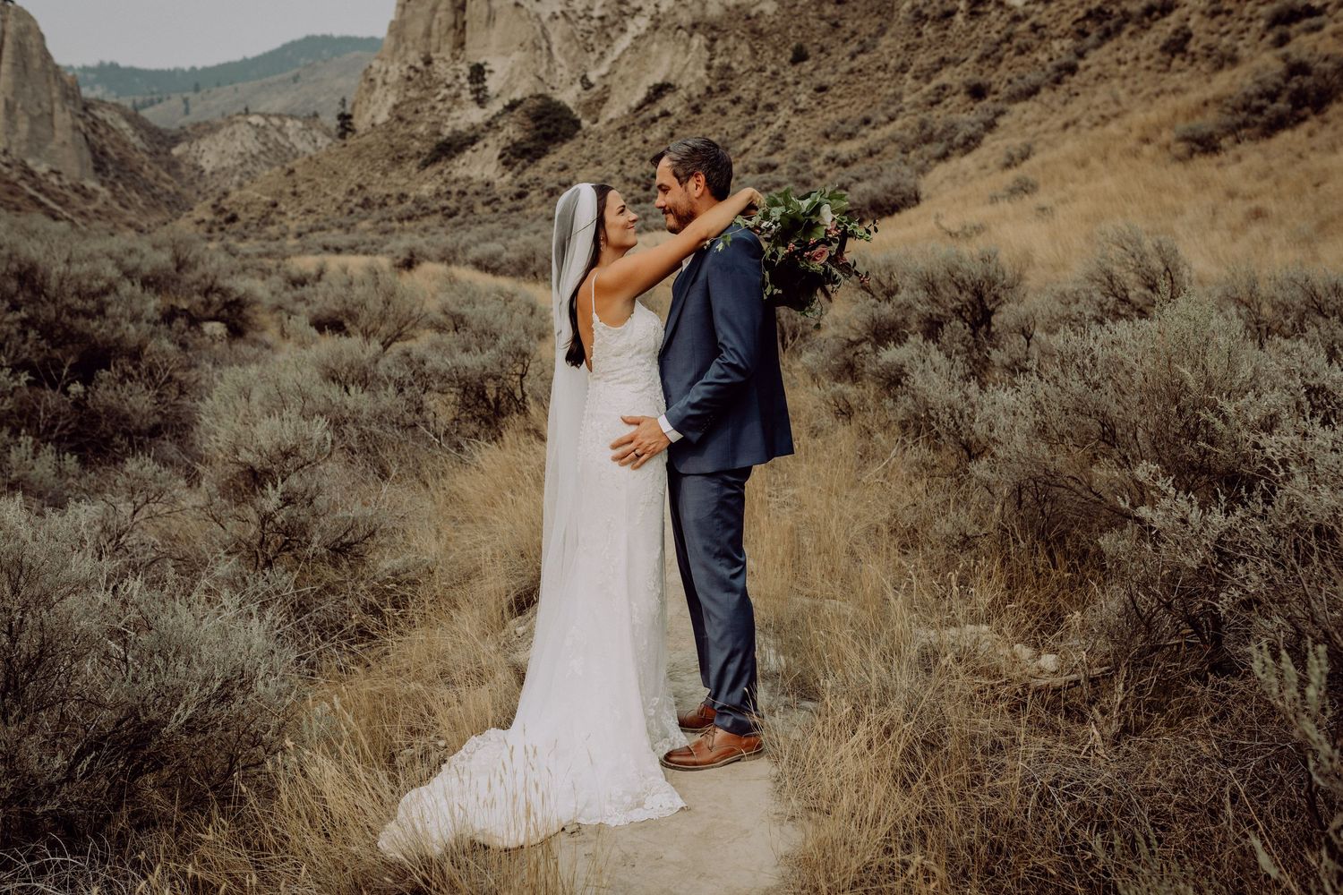 A couple embraces in a desert landscape with rugged mountains and sagebrush creating a romantic outdoor setting.