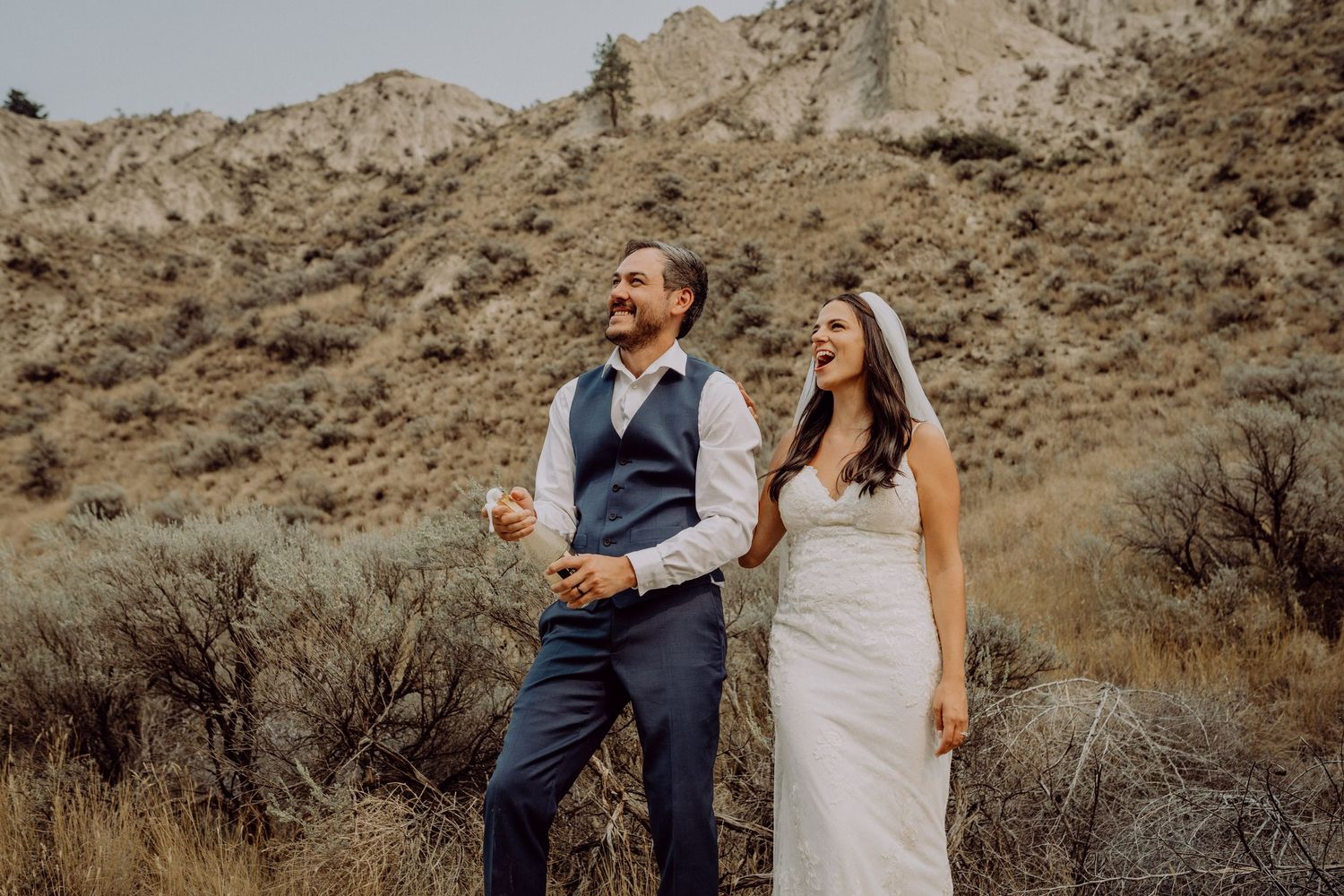 A couple in wedding attire shares romantic moments against a scenic desert mountain backdrop.
