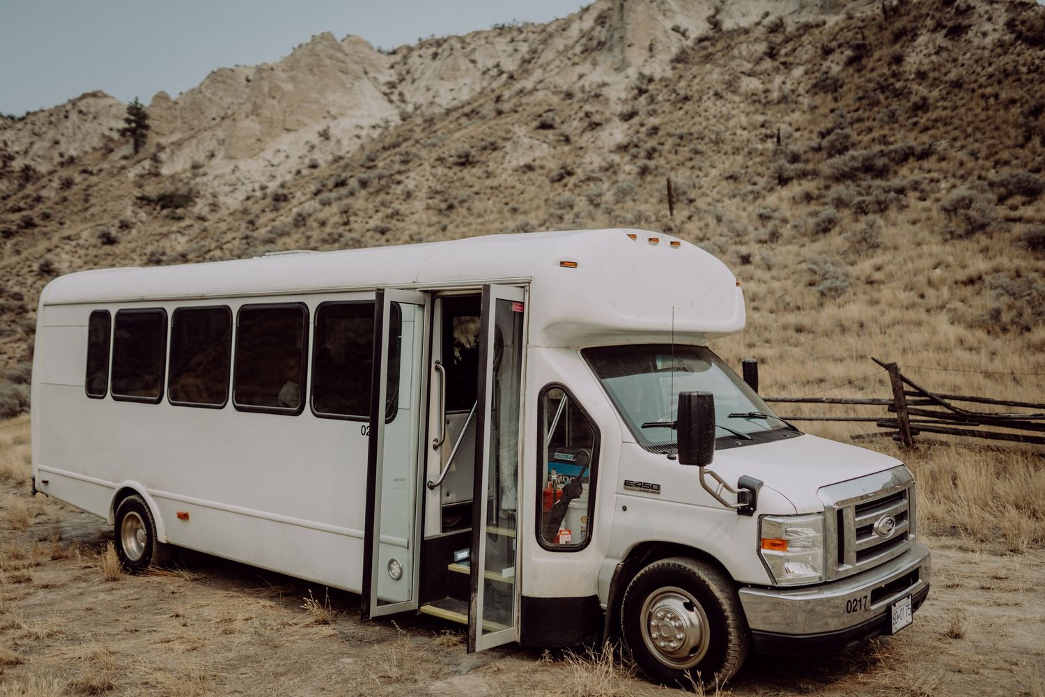 A white stretch limousine parked in a desert landscape with rocky hills in the background.