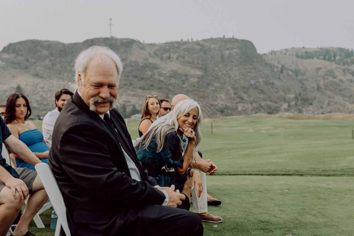 A group of people celebrating outdoors in a scenic mountain setting with green fields in the background.