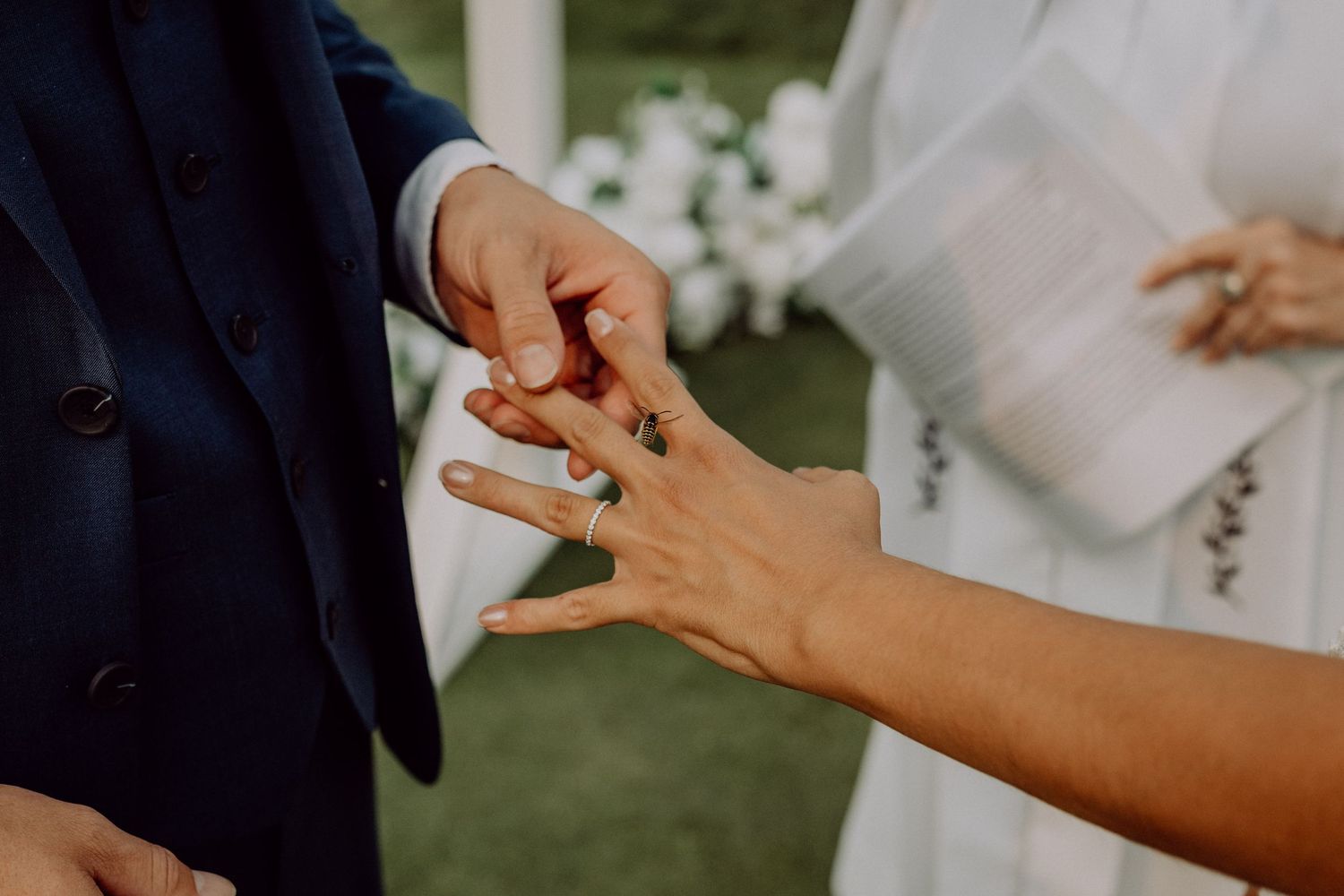 Close-up view of hands exchanging wedding rings during an outdoor ceremony.
