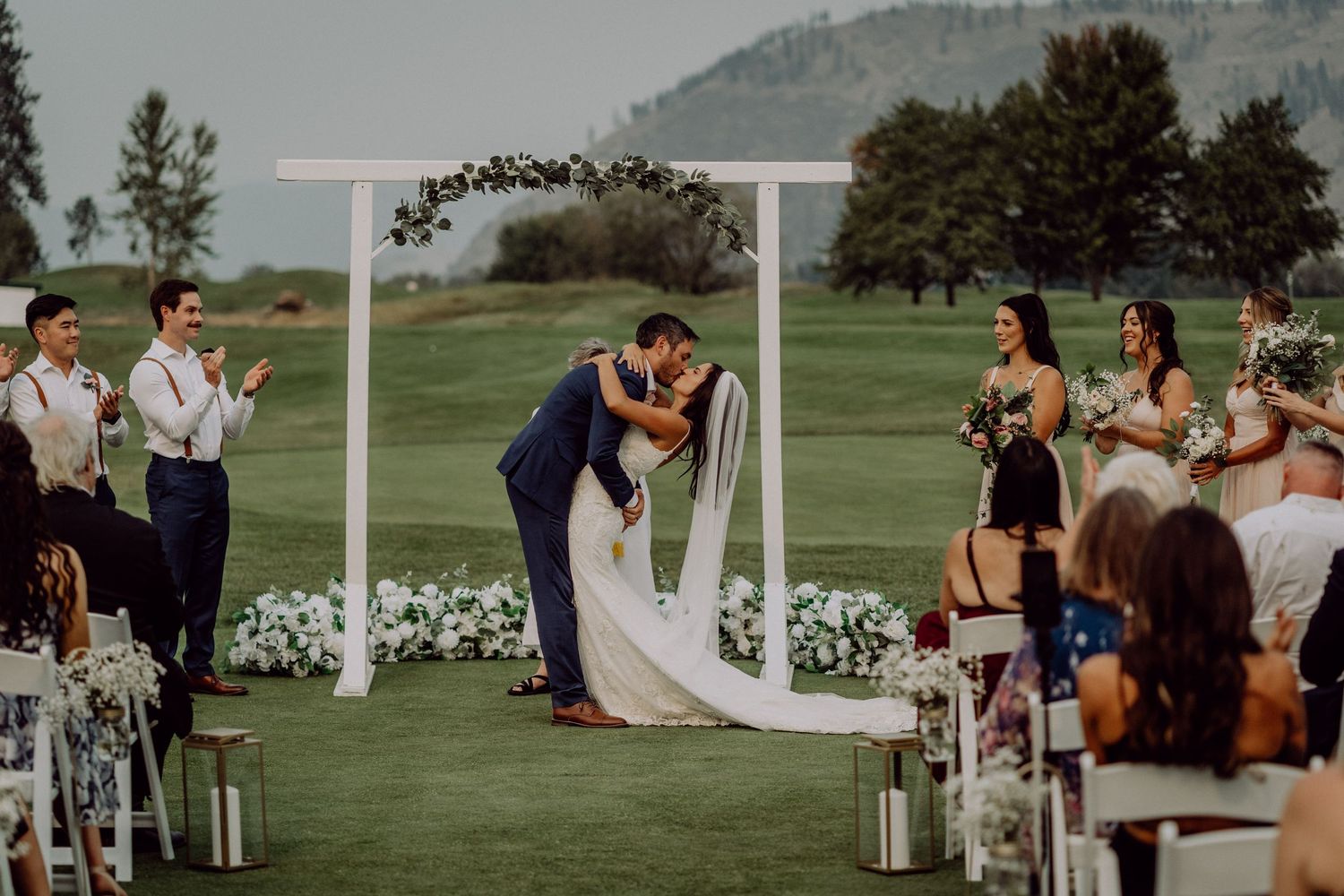 Scenic outdoor wedding ceremony setup on a lush green golf course with mountain views in the background.