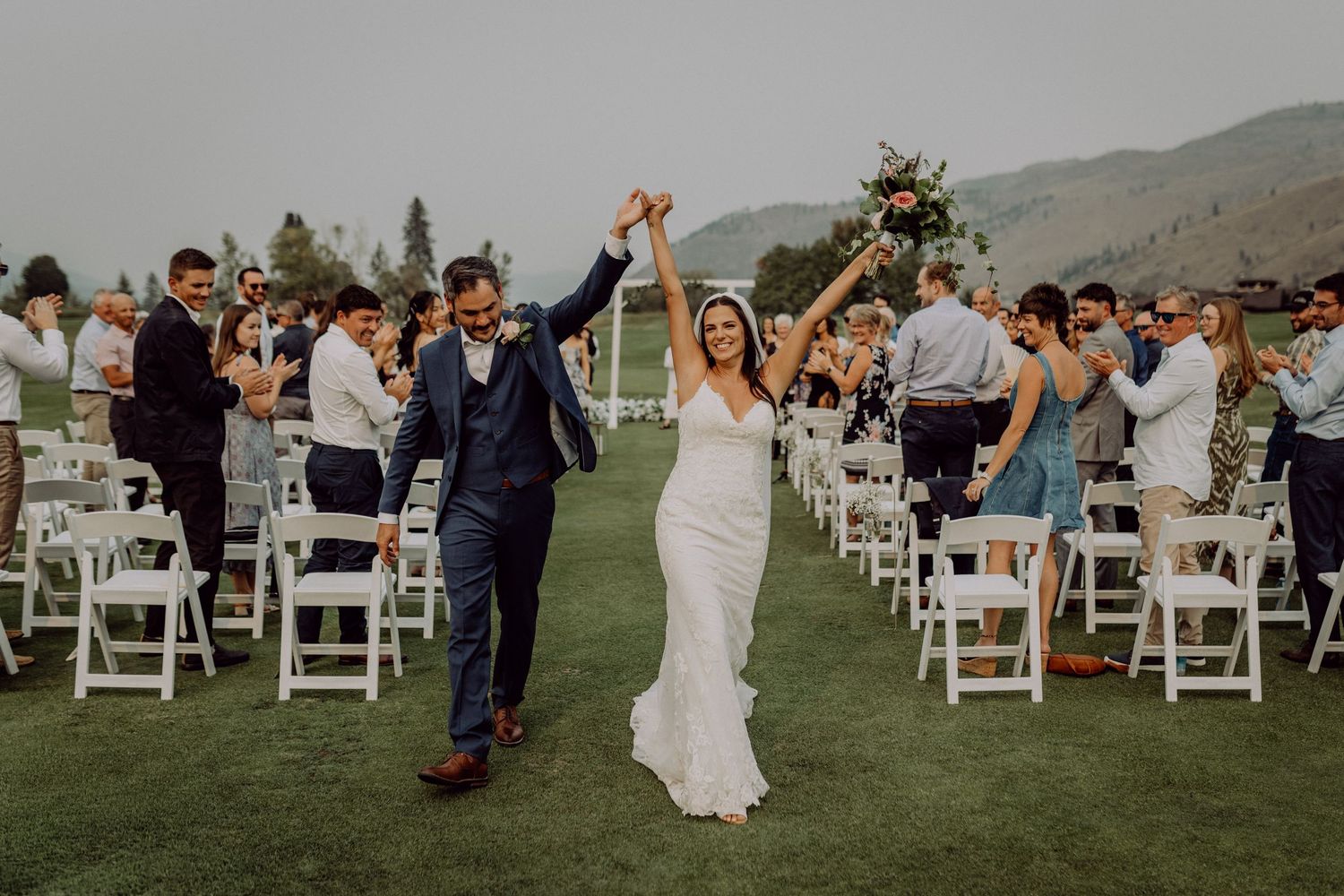 Wedding guests stand and dance during an outdoor celebration with mountain views in the background.