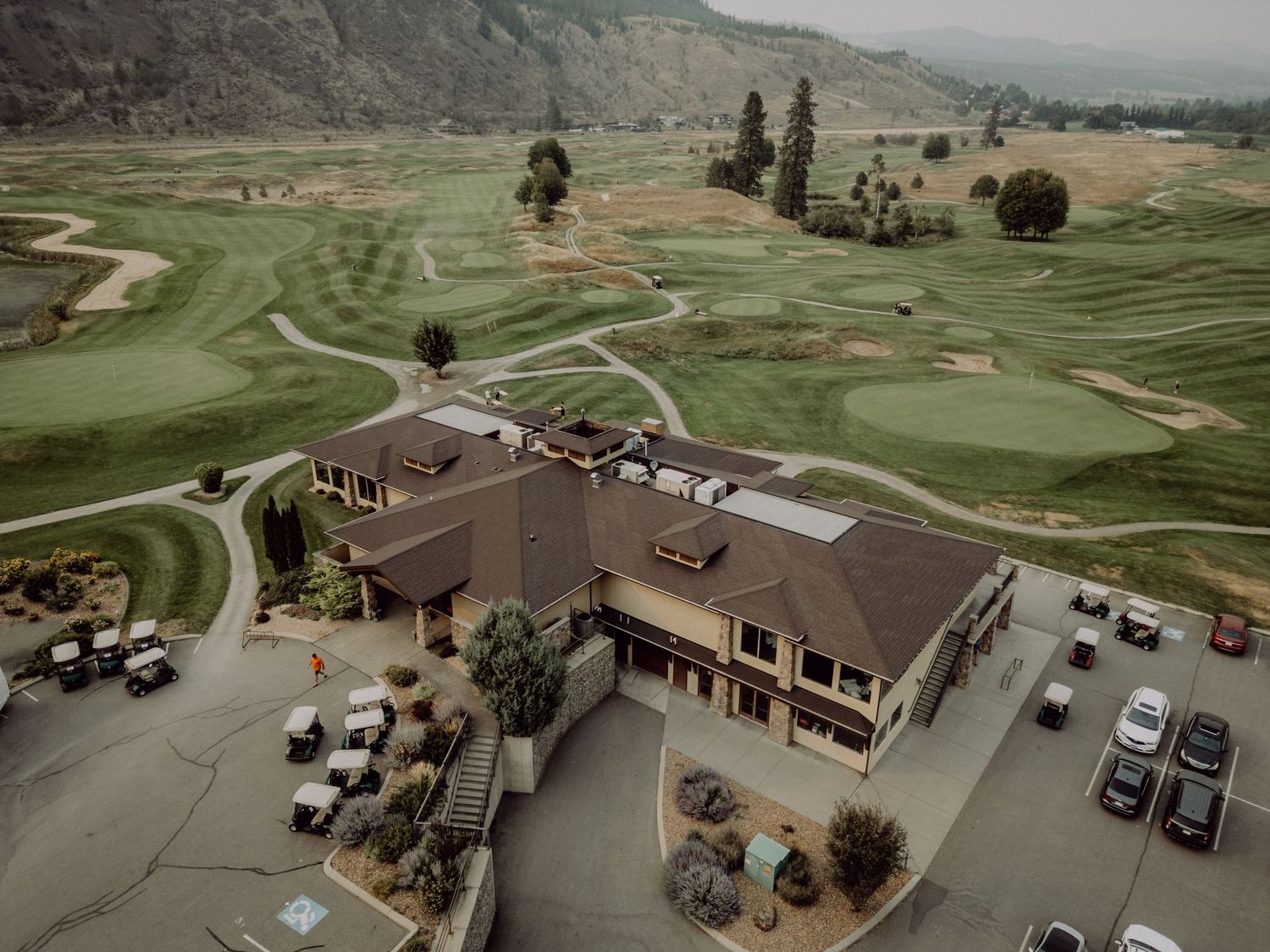 Aerial view of a golf course clubhouse with winding paths and green fairways nestled in mountainous terrain.