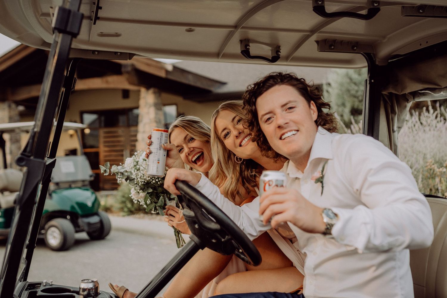 Three people smile together while sitting in a golf cart at a sunny outdoor venue.