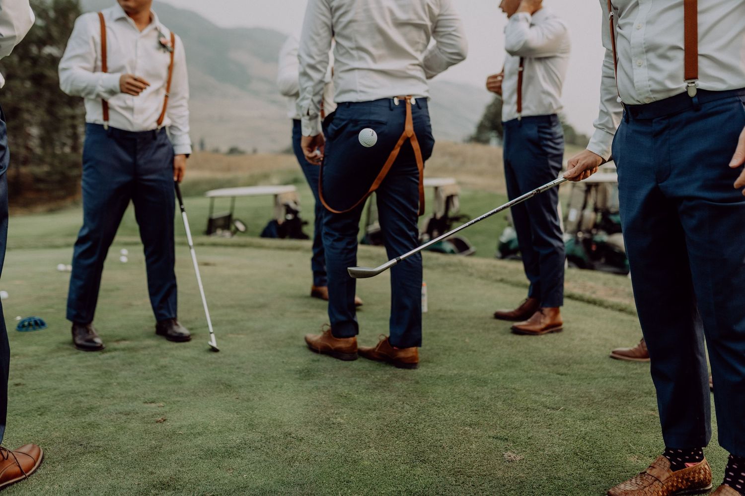 Wedding guests mingle on a grassy lawn during an outdoor reception with chairs arranged in rows.