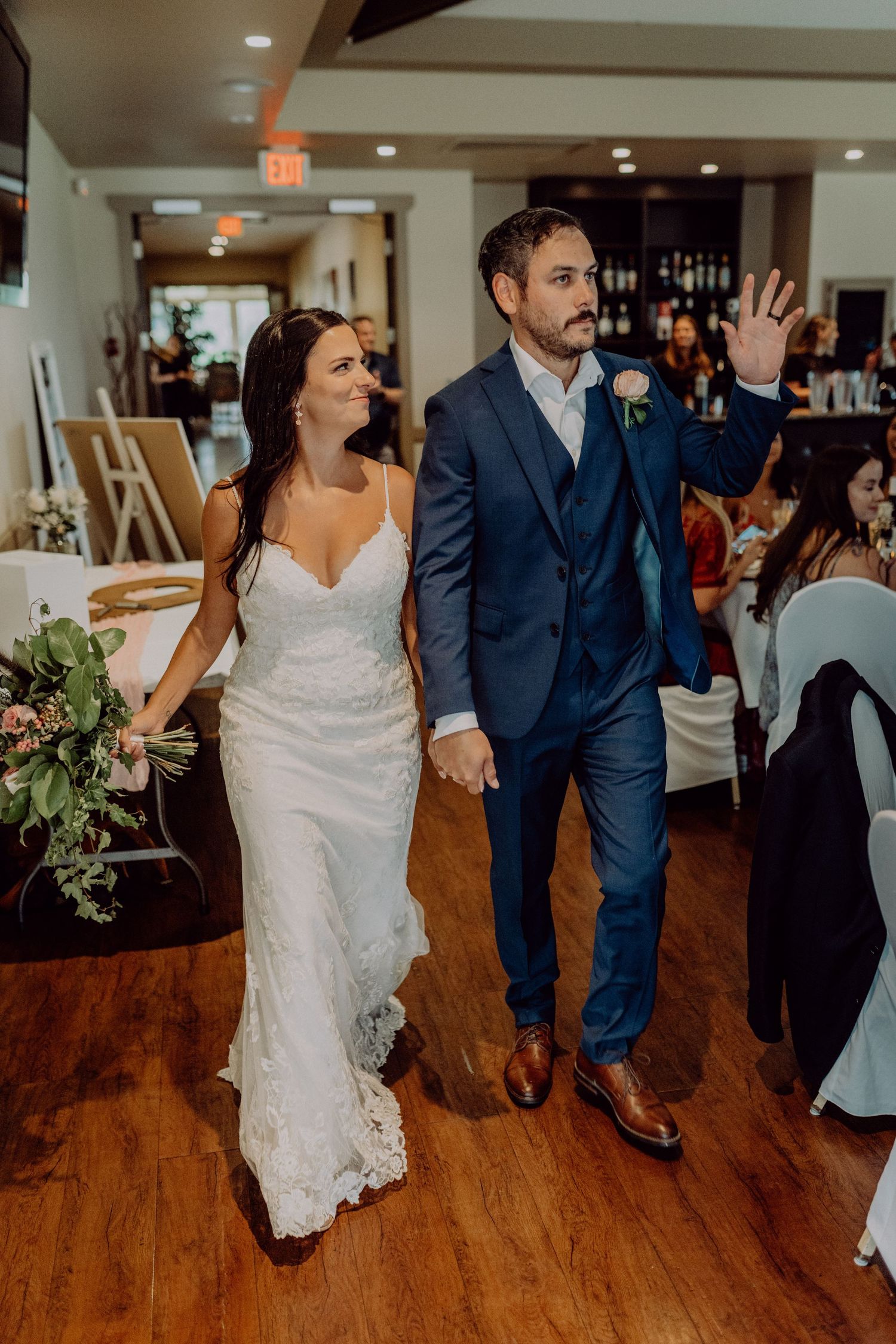 Newlyweds dance together at wedding reception on hardwood floor with guests watching in background.