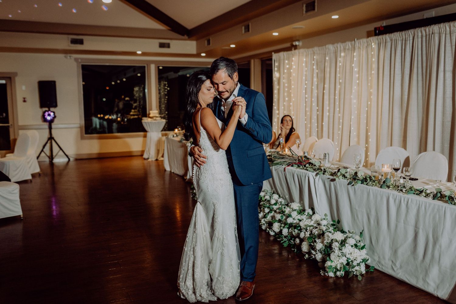 A couple shares their first dance at a wedding reception in an elegant ballroom with floral decorations.