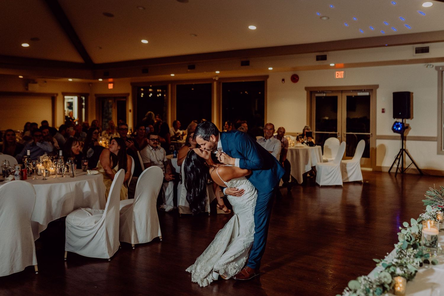 Couples dancing together on a dark wooden floor at an elegant wedding reception with soft lighting and white decor.