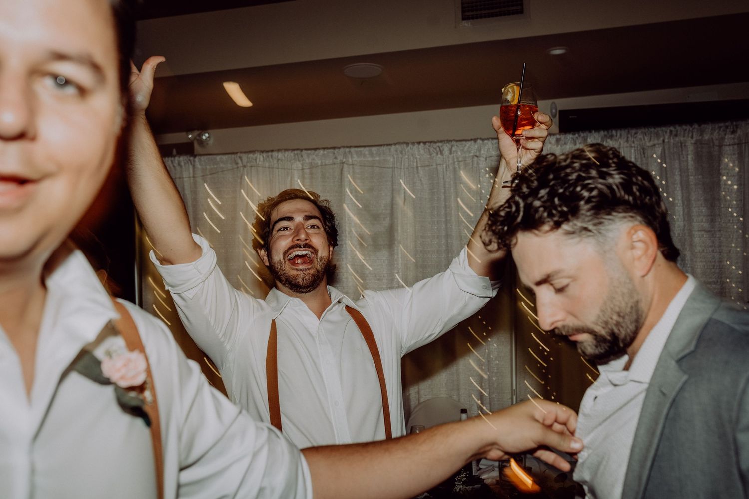 Wedding guests dance and celebrate joyfully on a crowded dance floor at an indoor reception.