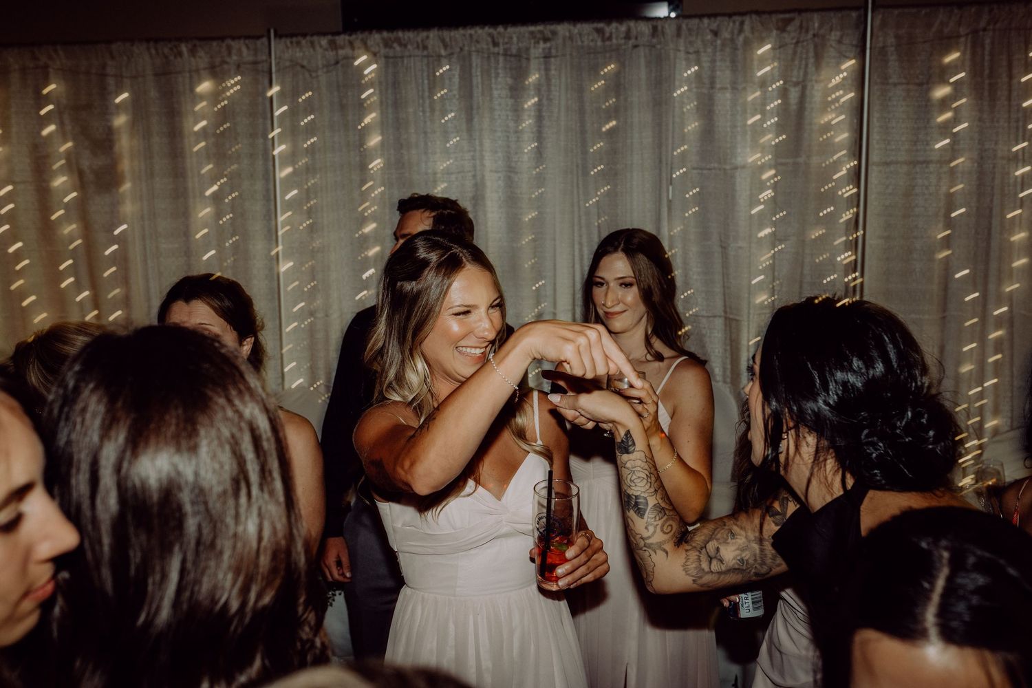 People dancing and celebrating at a wedding reception with string lights decorating the background.