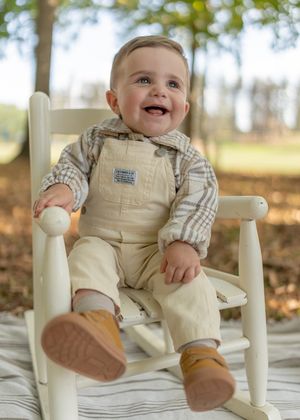 Baby sitting in white wooden chair during outdoor autumn photo session.