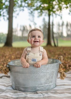 A baby sits happily in a galvanized metal tub during an outdoor photoshoot.